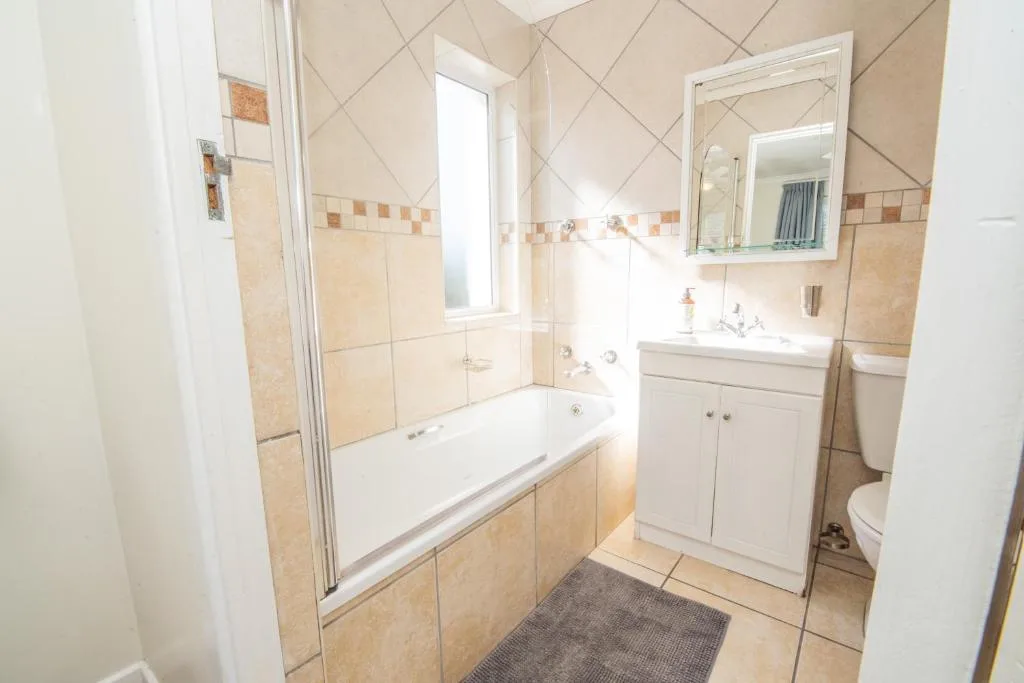 Bright bathroom with bathtub, vanity sink, mirror, and tiled walls