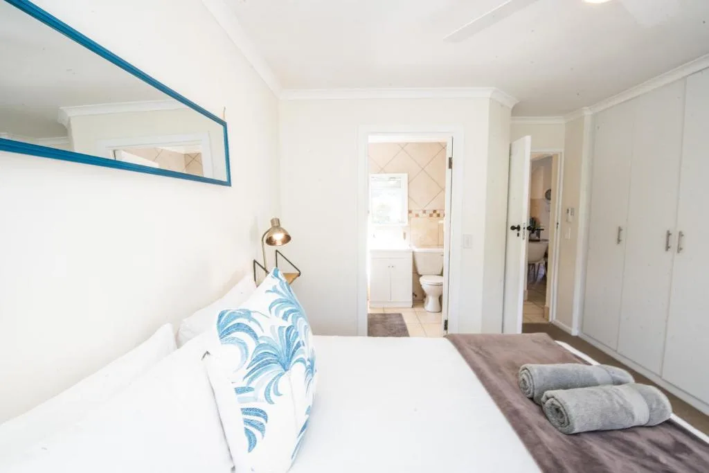 Bright bedroom with white bedding, blue patterned pillow, and ensuite bathroom visible through open door