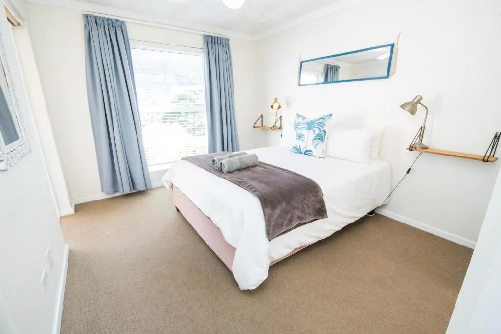 Bright bedroom with white bed, blue curtains, and ocean view window
