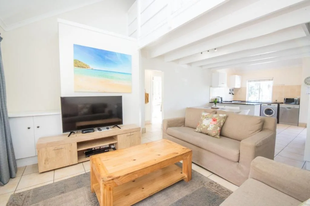 Bright open-plan lounge with beige sofa, wooden coffee table, and TV