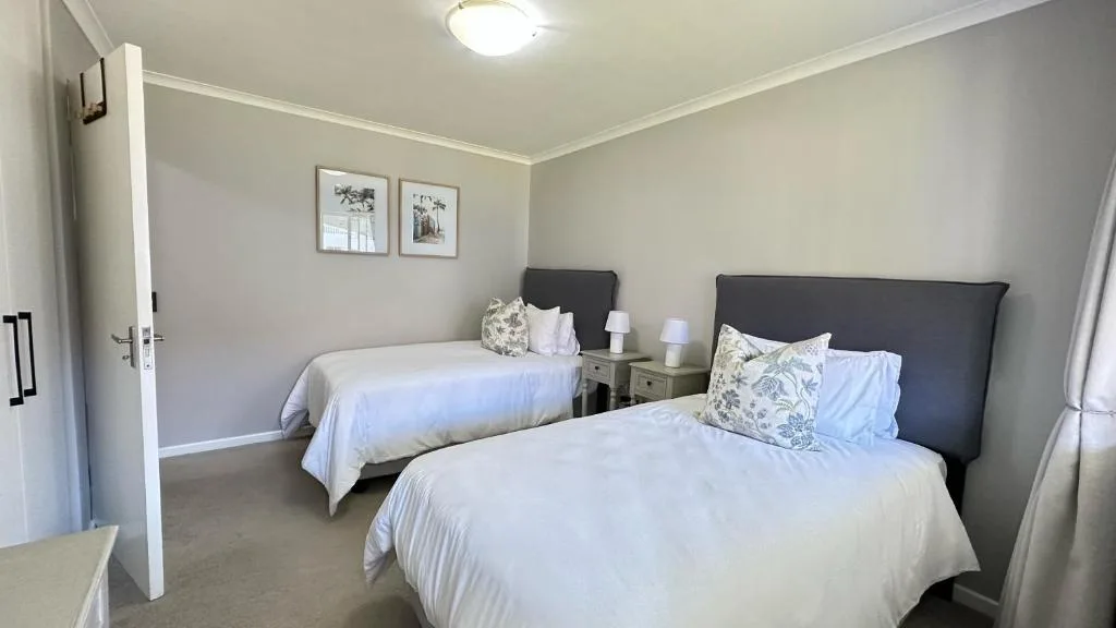 Spacious bedroom with two single beds, dark headboards, and neutral décor