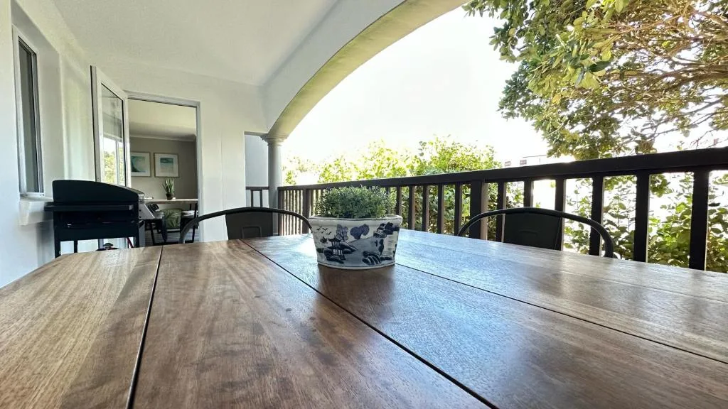 Covered wooden deck with dining table overlooking lush garden vegetation