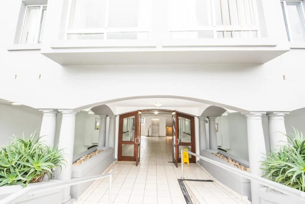 Modern white building entrance with columned portico and potted plants