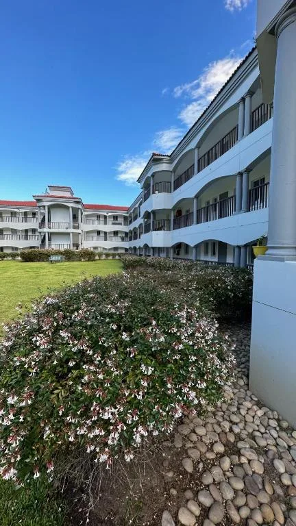 Multi-story white apartment building with balconies and flowering garden beds