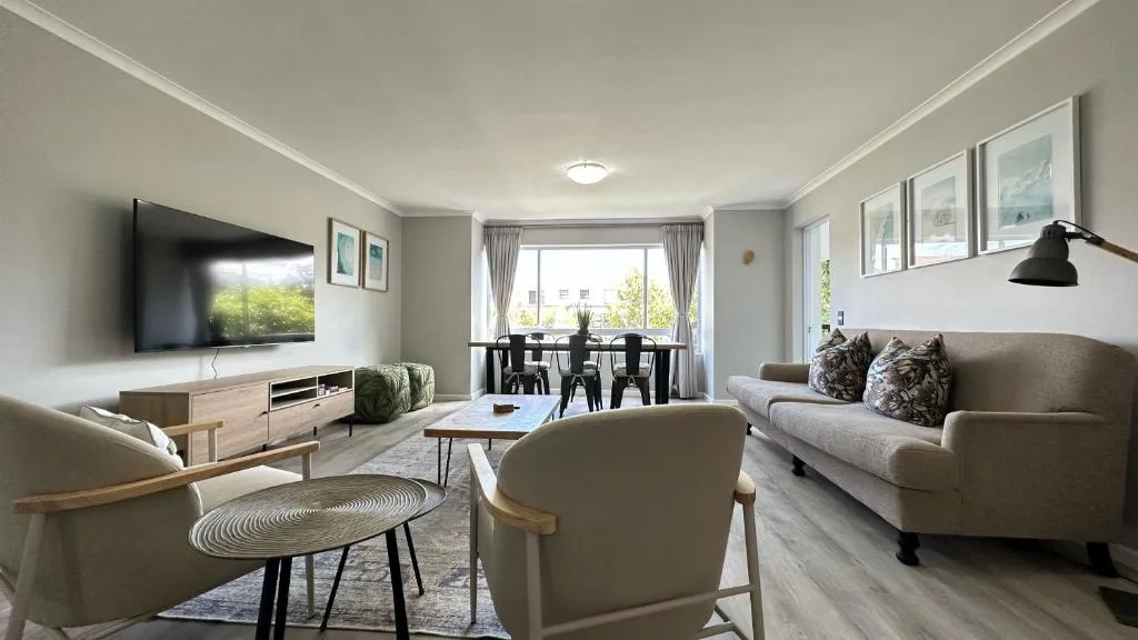 Modern lounge with grey sofas, TV, and dining area visible beyond