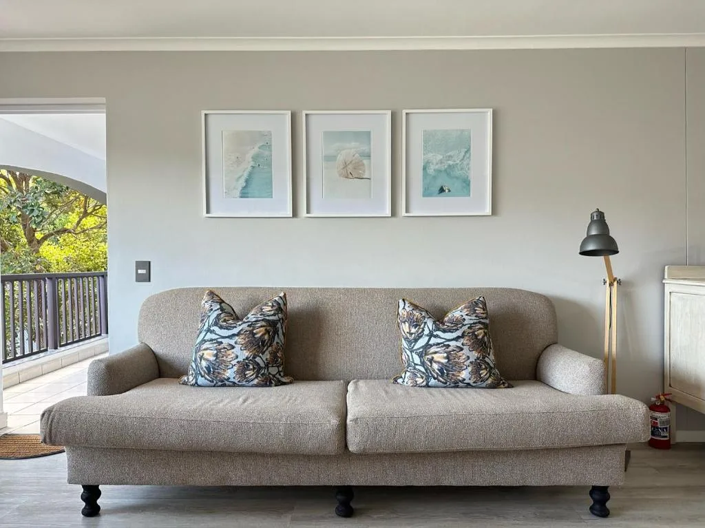 Spacious lounge with gray sofa, patterned pillows, and coastal artwork above