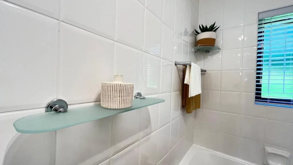 Modern white bathroom with glass shelf, decorative plant, and folded towels