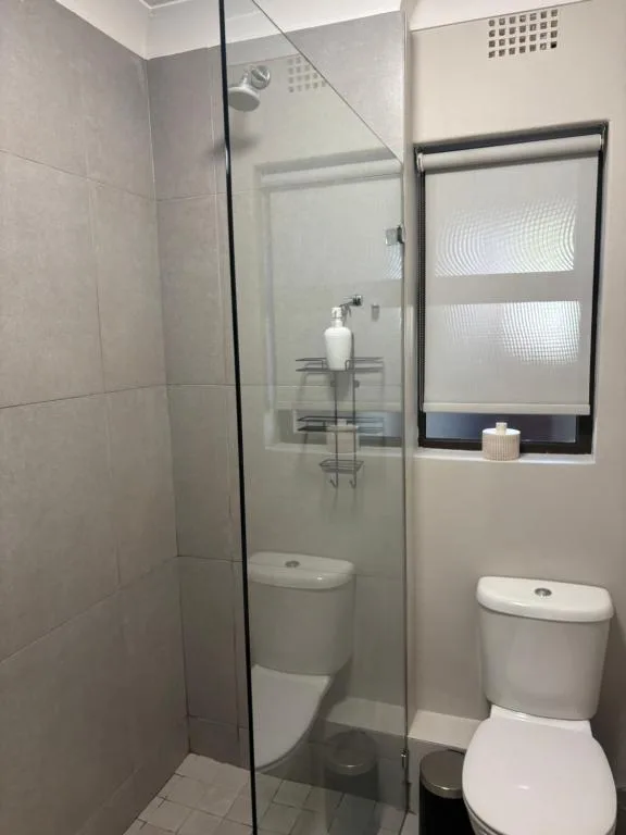 Modern bathroom with walk-in shower, toilet, and window with blinds