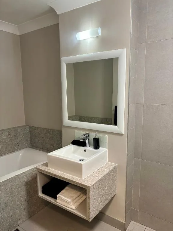 Modern bathroom with illuminated mirror, white square sink, and neutral tile walls