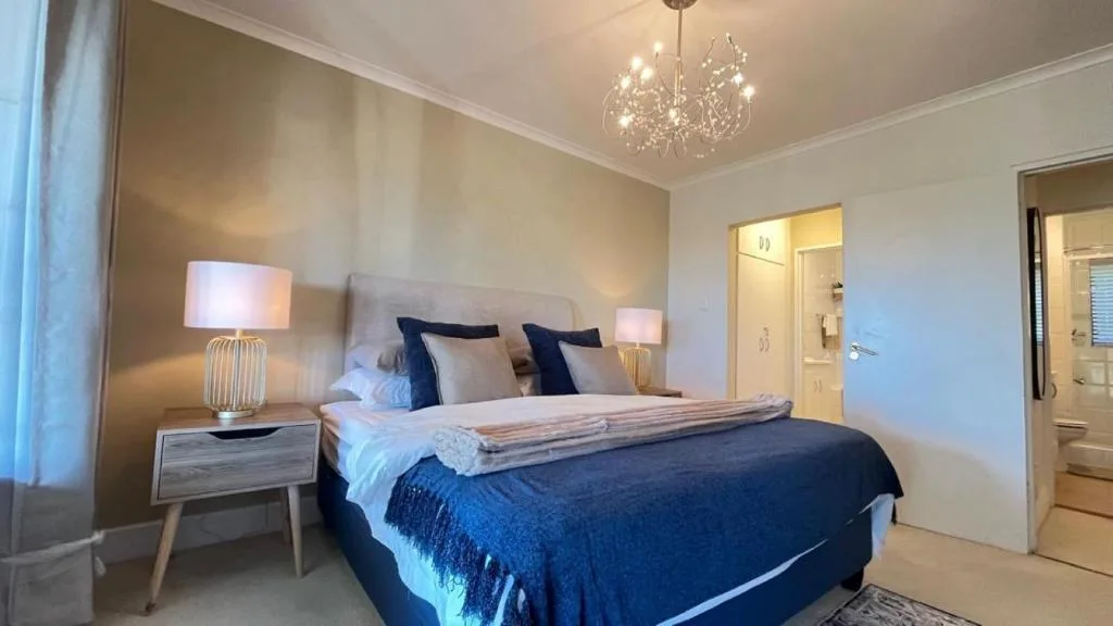 Elegant bedroom with queen bed, navy bedding, pendant chandelier, and ensuite access