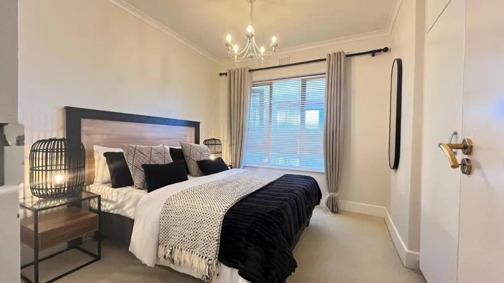 Modern bedroom with queen bed, black headboard, elegant chandelier, and garden views