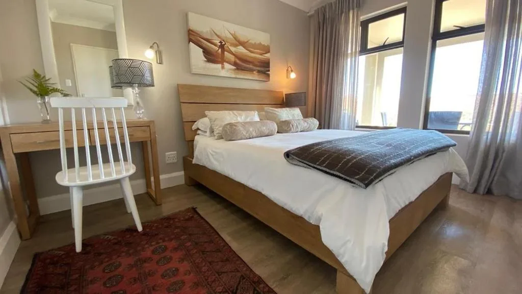 Spacious bedroom with wooden bed frame and white linens overlooking garden view