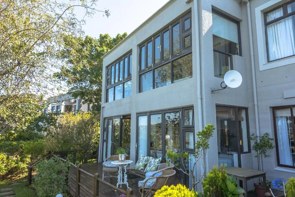 Modern white apartment building with large windows and outdoor seating area surrounded by greenery