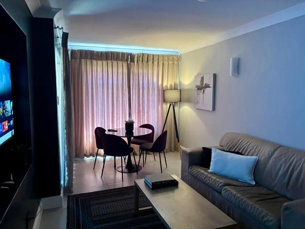 Modern lounge with gray sofa, TV, and contemporary dining area by curtains