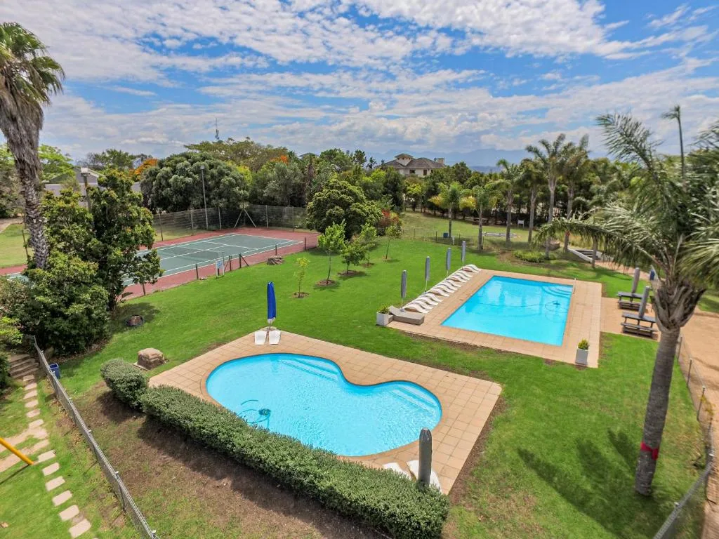 Aerial view of two swimming pools, tennis court, lush gardens and palm trees