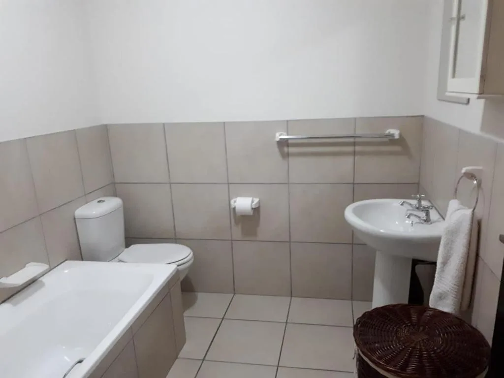 Clean bathroom with toilet, bathtub, pedestal sink and tiled walls