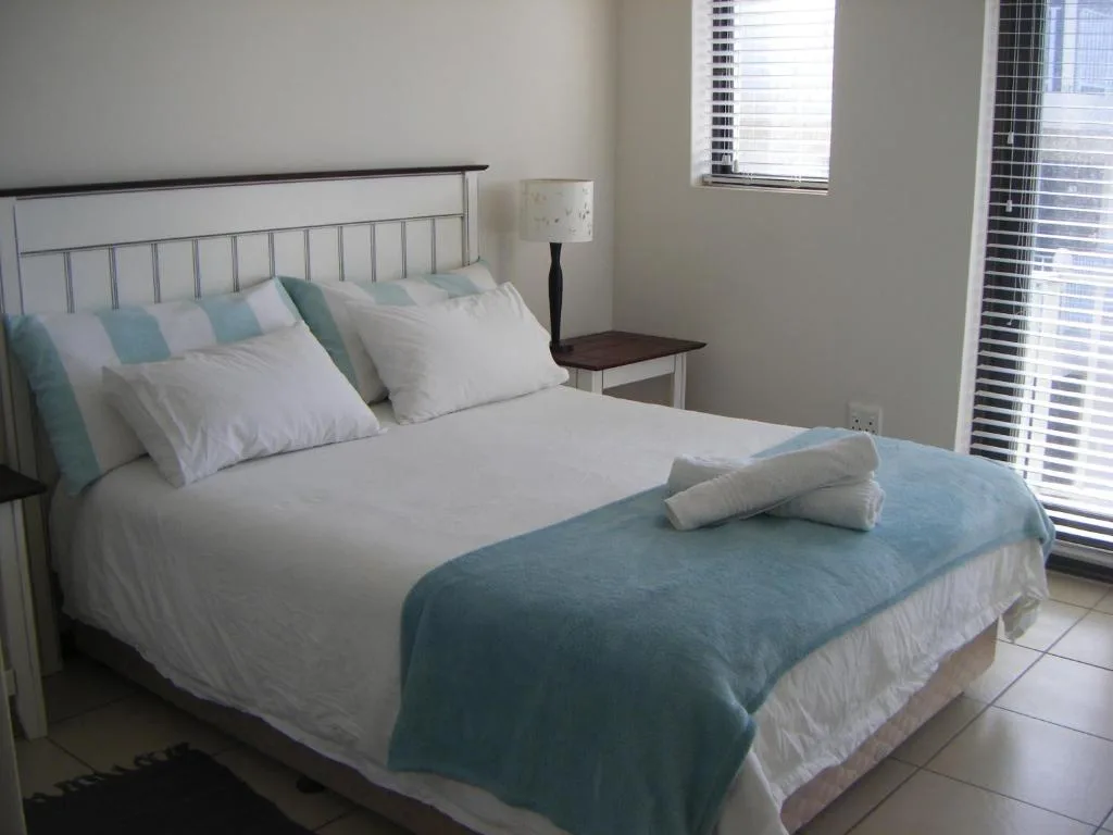 Bright bedroom with made double bed, striped pillows, and side table lamp