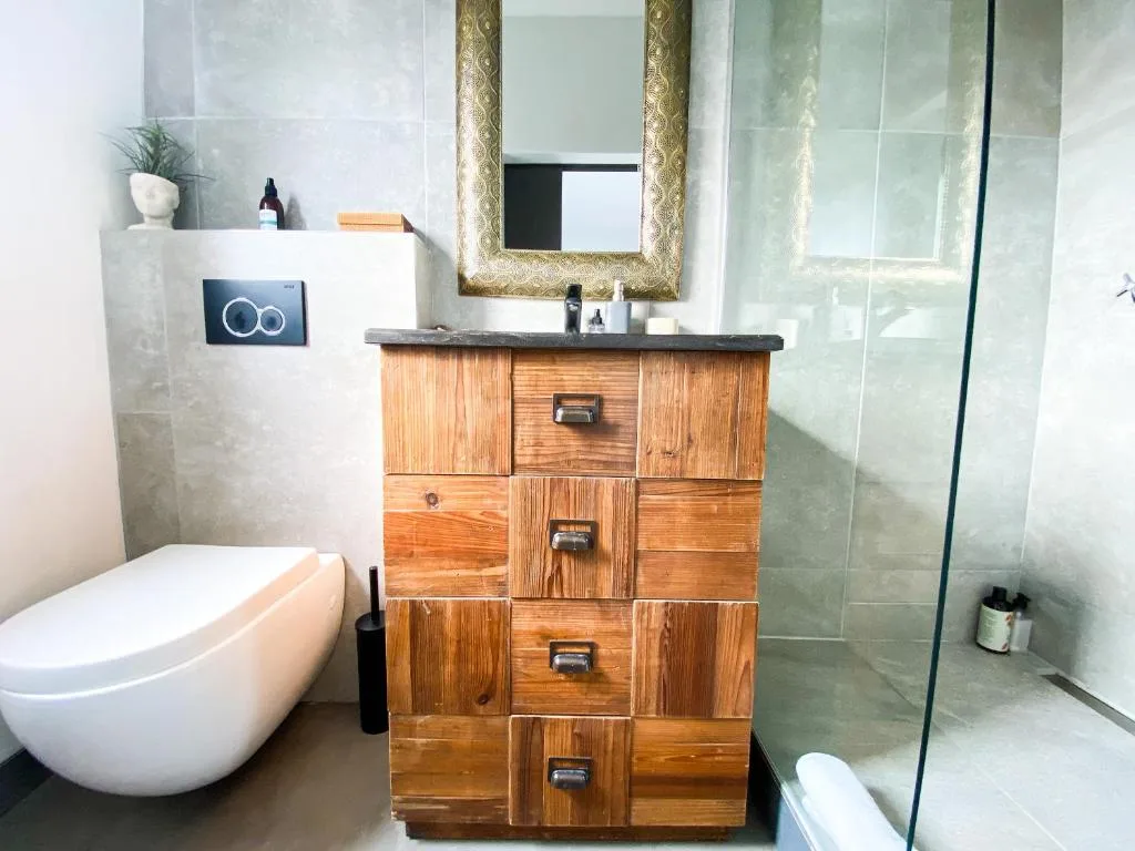 Modern bathroom with wooden vanity, gold-framed mirror, and walk-in shower
