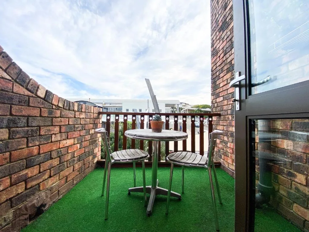 Compact rooftop patio with artificial turf, dining table, and brick walls