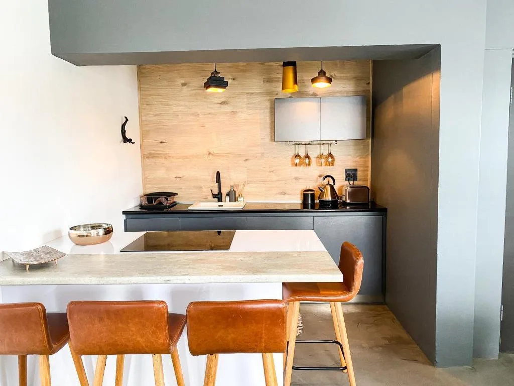 Modern kitchen with wooden backsplash, black counters, pendant lights, and bar seating