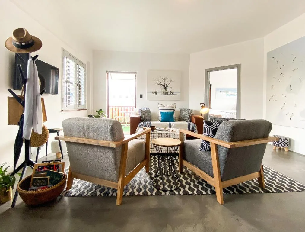 Bright living room with gray armchairs, wooden frames, geometric rug, coastal decor
