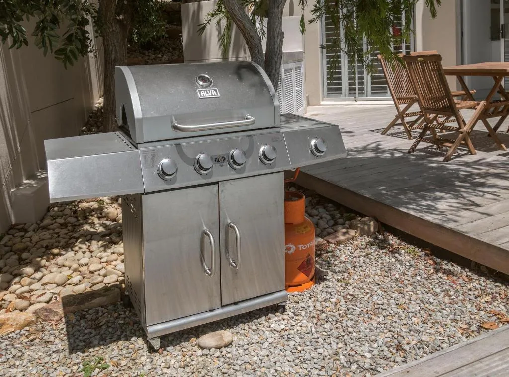 Stainless steel gas braai grill on patio with wooden deck chairs
