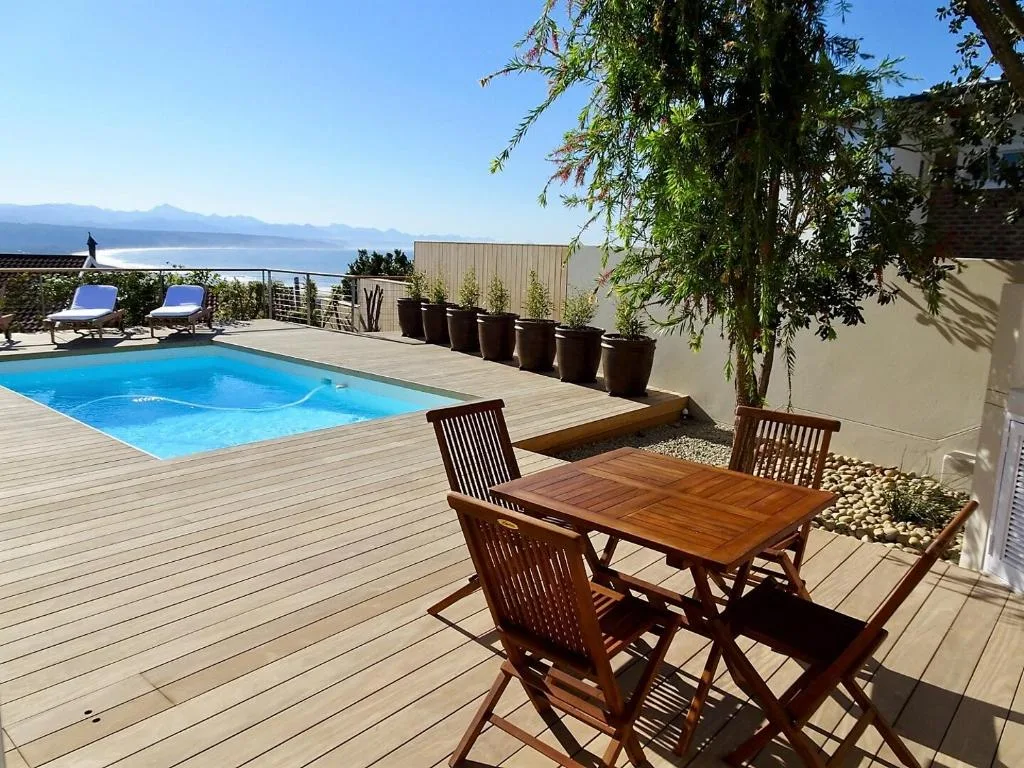 Wooden deck with dining table, pool, and mountain lagoon views