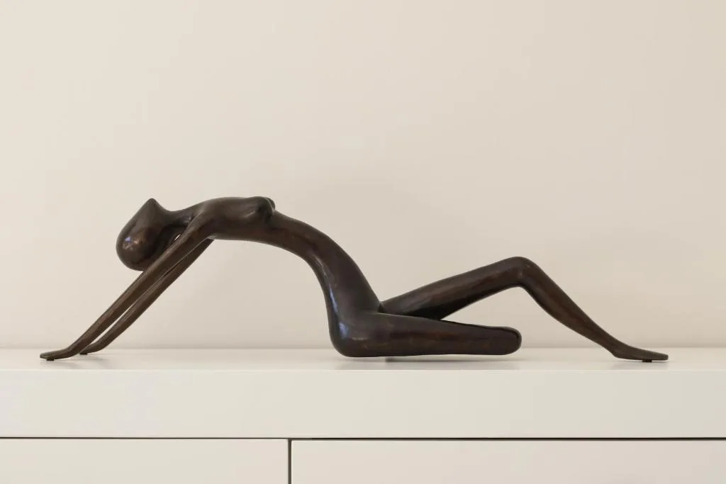 Modern bronze sculptural figure displayed on white interior shelf