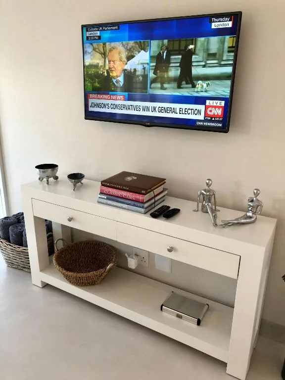 Wall-mounted television above white console table with decorative items and storage