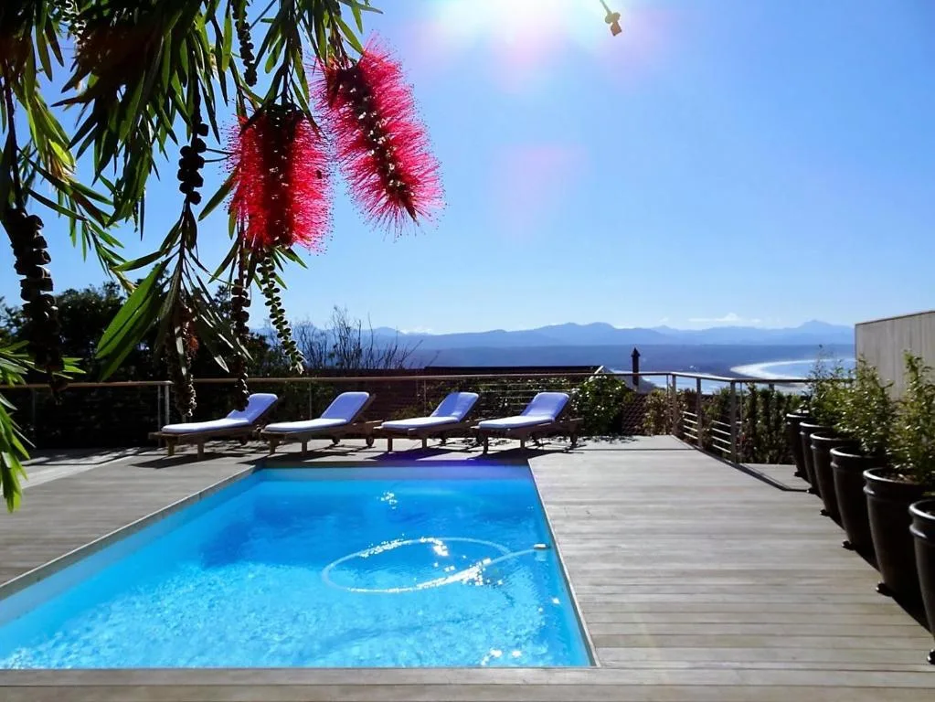 Sparkling blue swimming pool on wooden deck with mountain and lagoon views