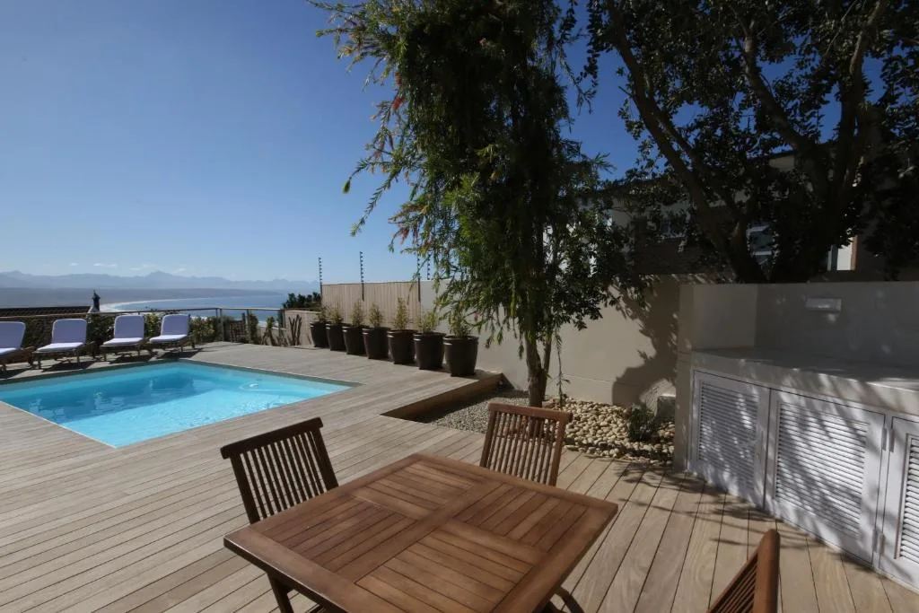 Wooden deck with swimming pool, dining table, and ocean views beyond