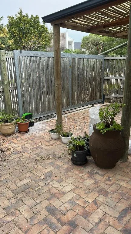 Sheltered patio area with wooden pergola, potted plants, and brick paving
