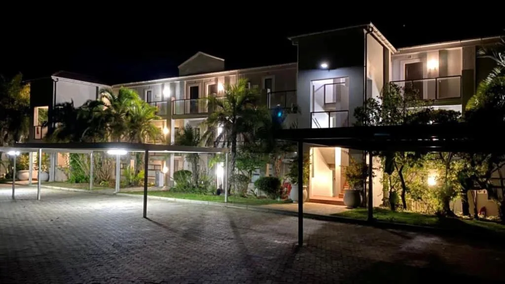 Modern apartment complex at night with illuminated facade and manicured gardens