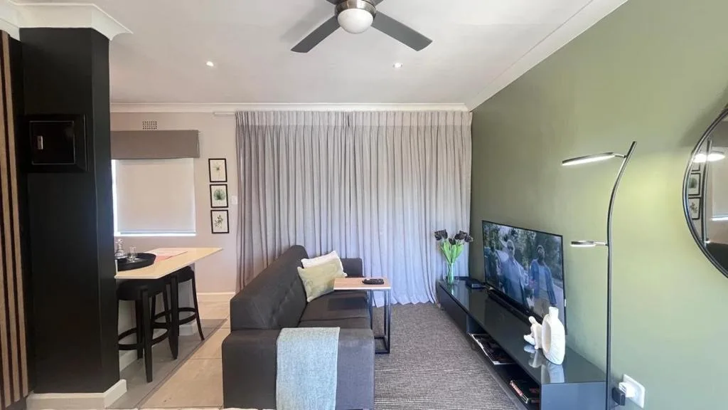 Modern lounge with charcoal sofa, TV, and kitchenette visible in background