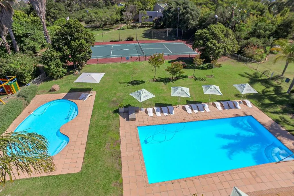 Two bright blue swimming pools with loungers and umbrellas on brick terrace