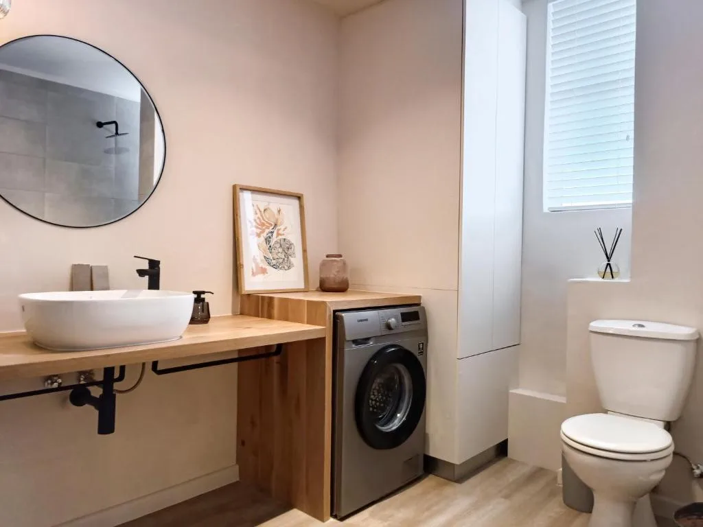 Modern bathroom with round sink, mirror, toilet, and washing machine