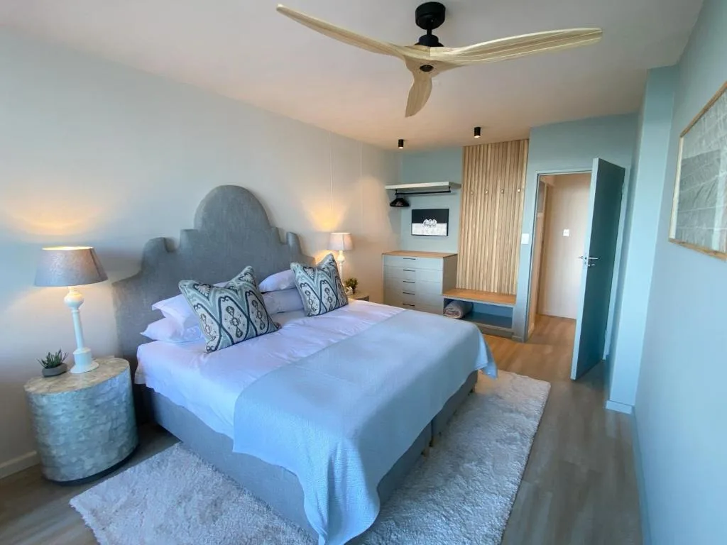 Modern bedroom with queen bed, blue headboard, patterned pillows, and ceiling fan