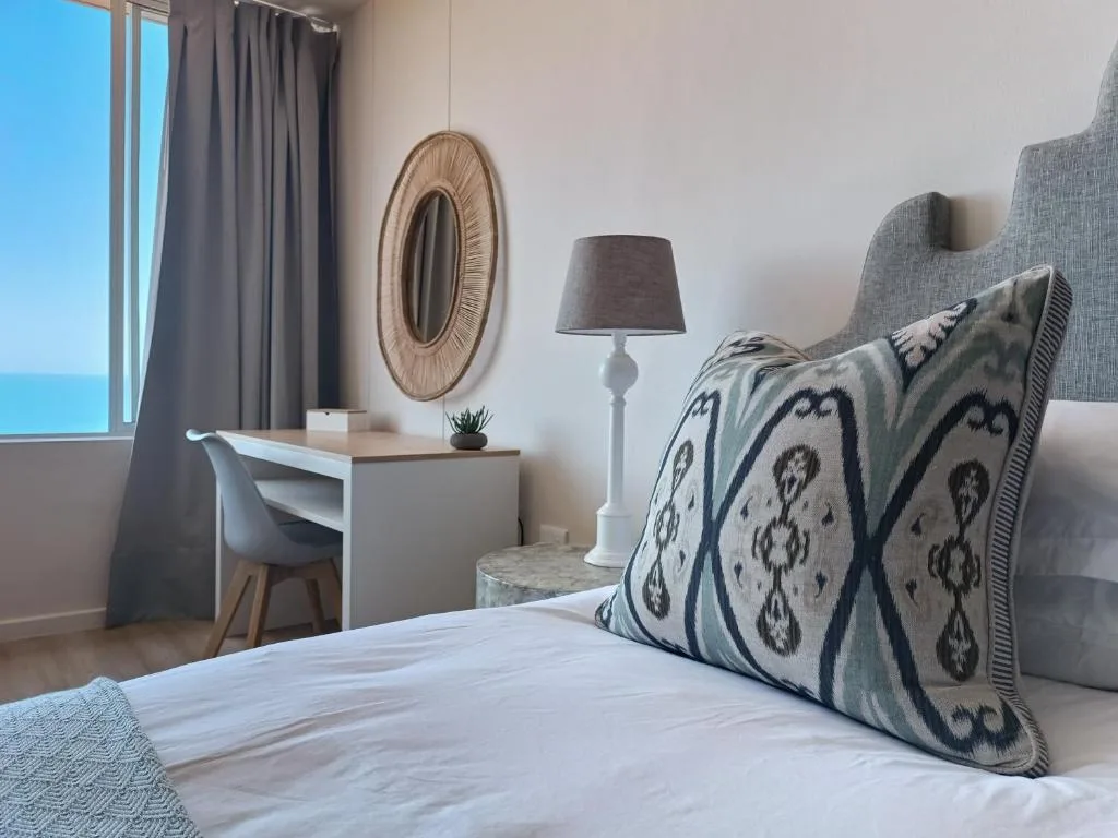 Coastal bedroom with patterned pillows, desk, and ocean view through window