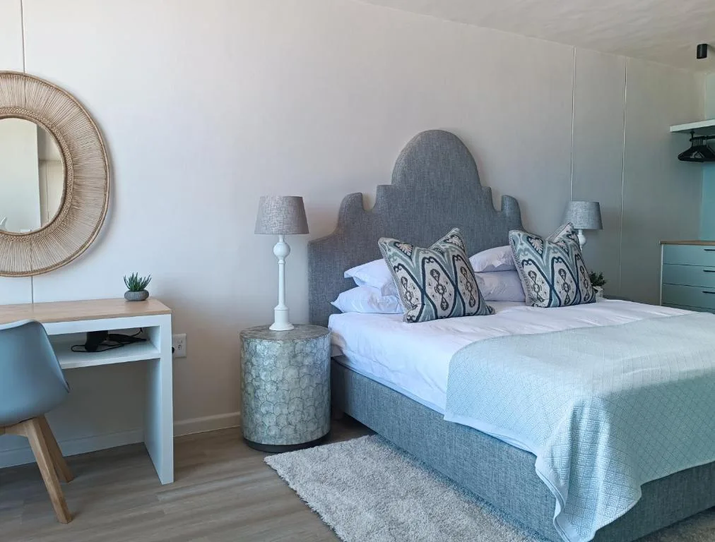 Modern bedroom with gray upholstered bed, patterned pillows, and desk