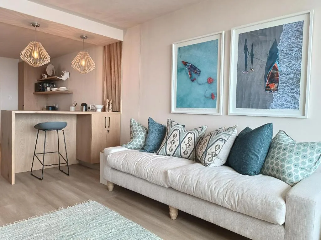 Open-plan lounge with cream sofa, coastal artwork, and integrated kitchenette