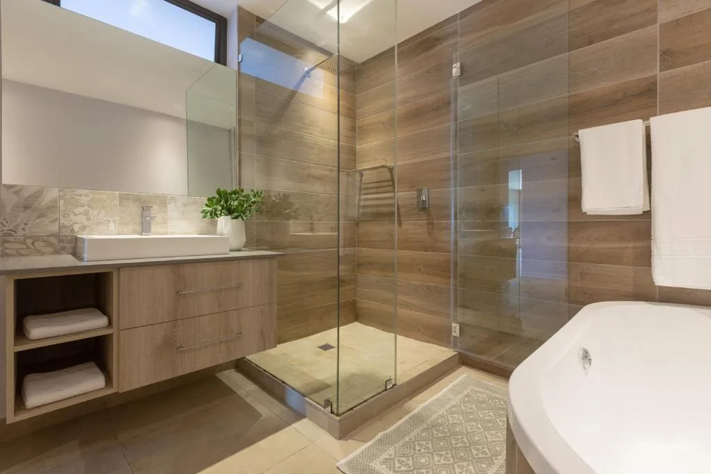 Modern bathroom with wooden tile walls, glass shower enclosure, and freestanding bathtub