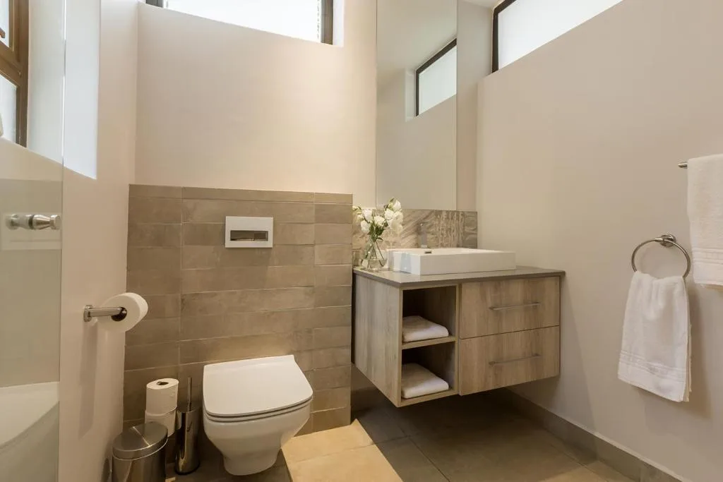 Modern bathroom with wooden vanity, round white sink, and tiled shower area