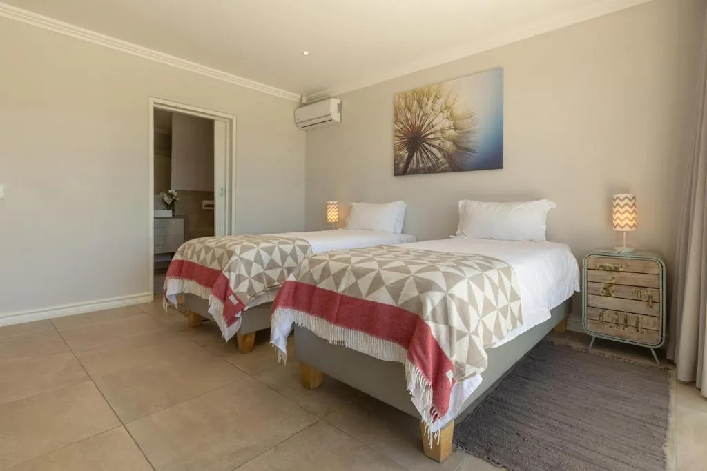Twin beds with patterned throws in bright, airy bedroom with ensuite