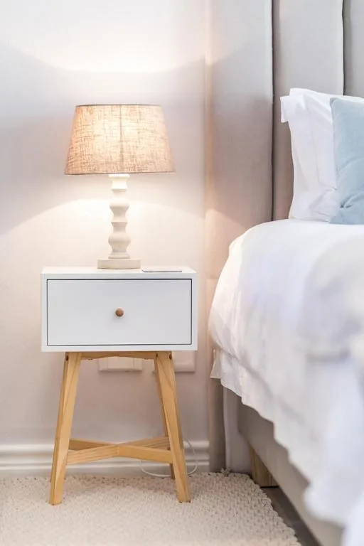 Modern bedroom bedside table with warm lamp and white linens