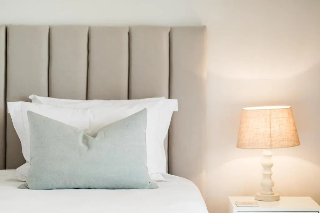 Modern bedroom with upholstered headboard, white linens, and bedside lamp