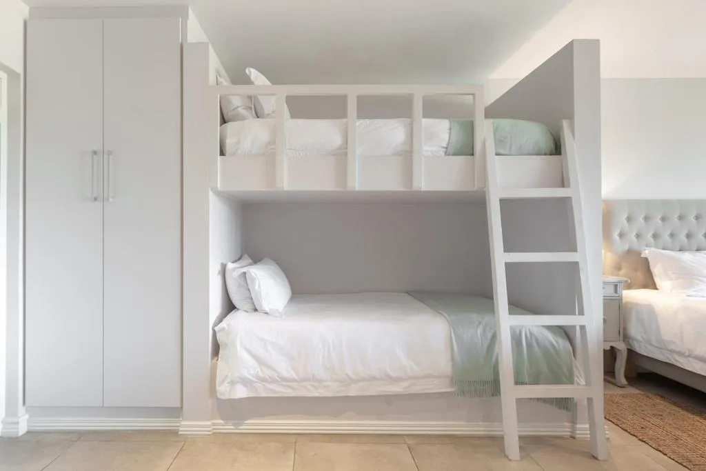 Modern white bunk bed with built-in storage and ladder in bright bedroom