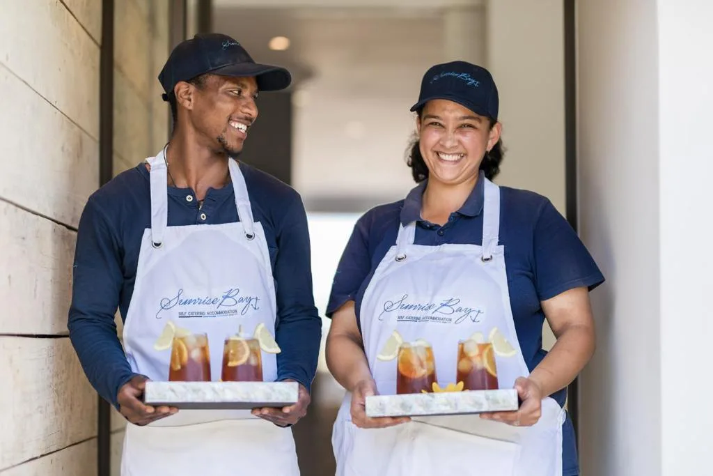 Smiling staff members in branded aprons holding refreshment trays indoors