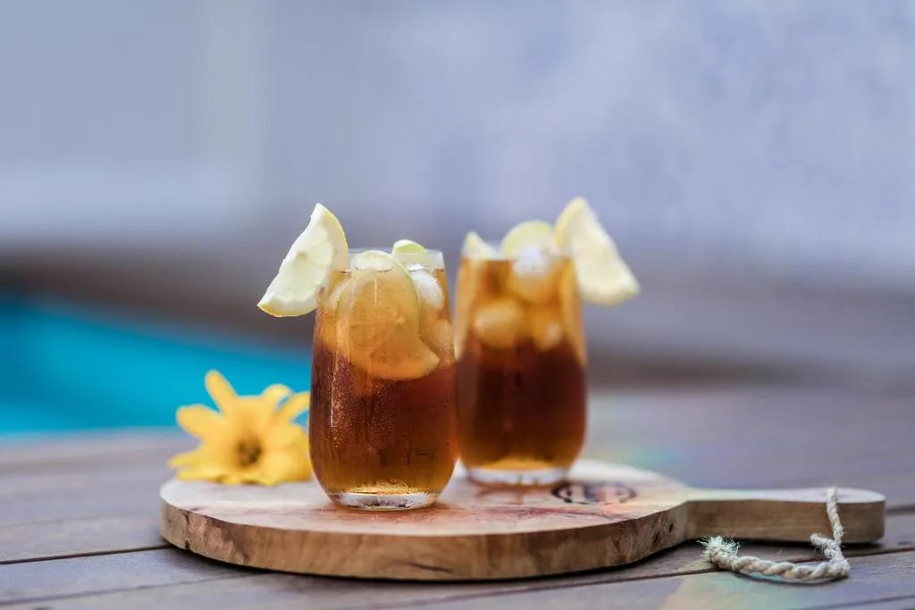 Refreshing cold drinks with lime garnish on wooden board by pool