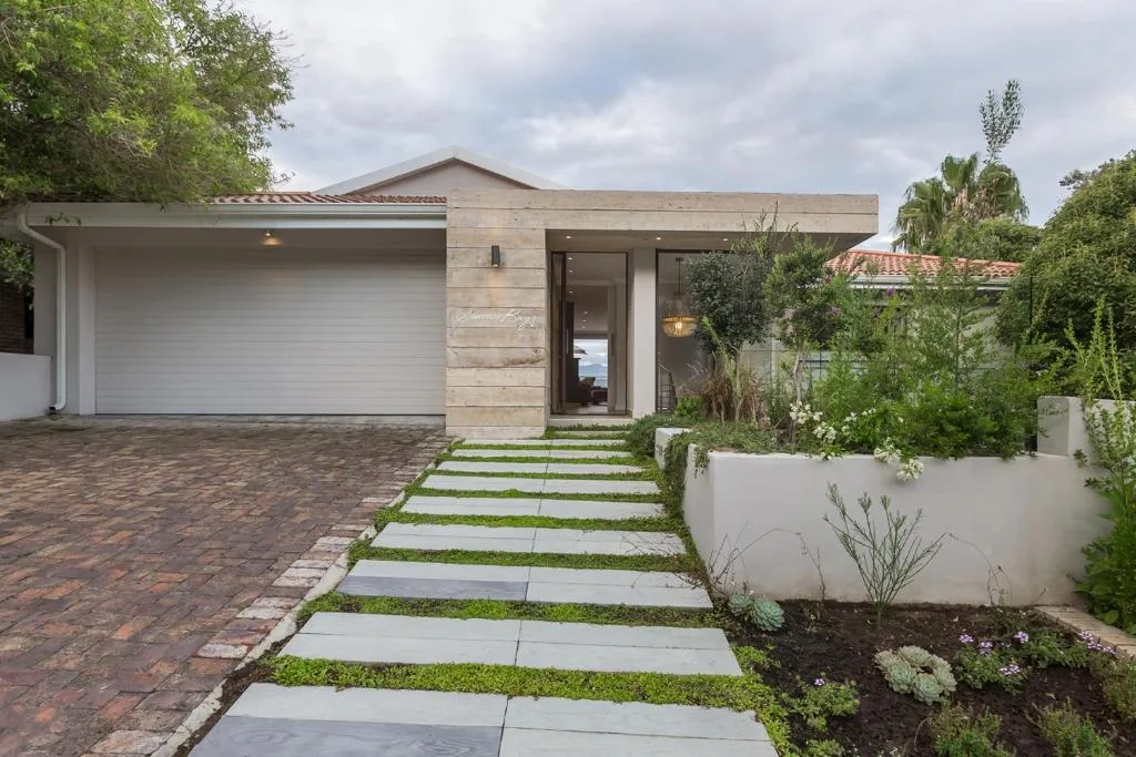 Modern home entrance with white garage, stone facade, and landscaped front garden
