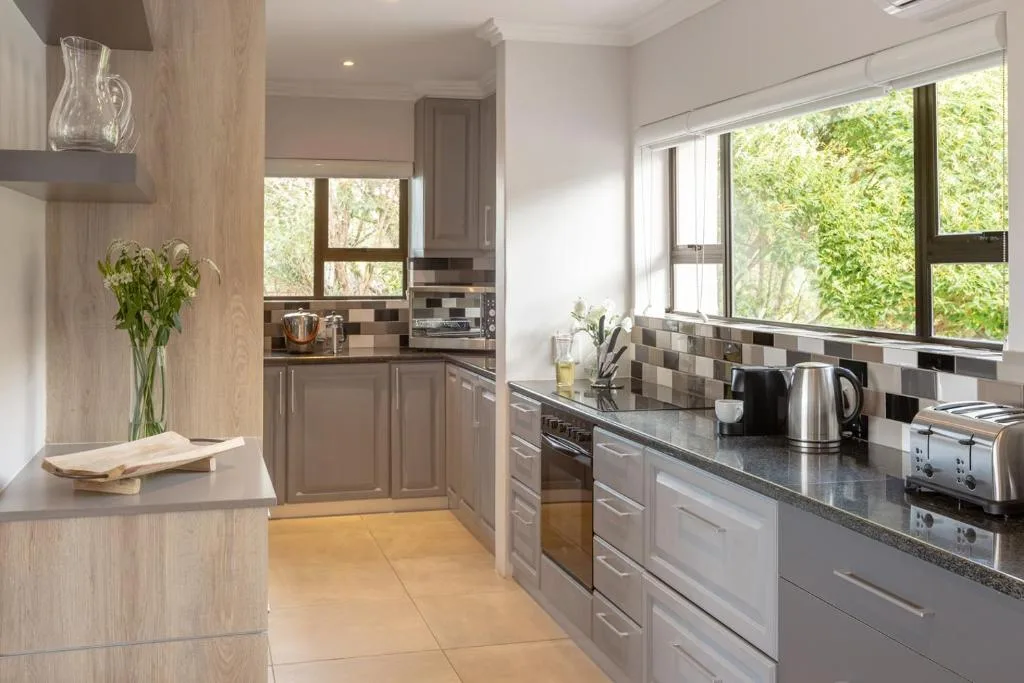 Modern kitchen with grey cabinetry, dark countertops, stainless steel appliances, and garden views